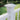 White square post cap on a white railing with green grass and bushes in the background #color_white