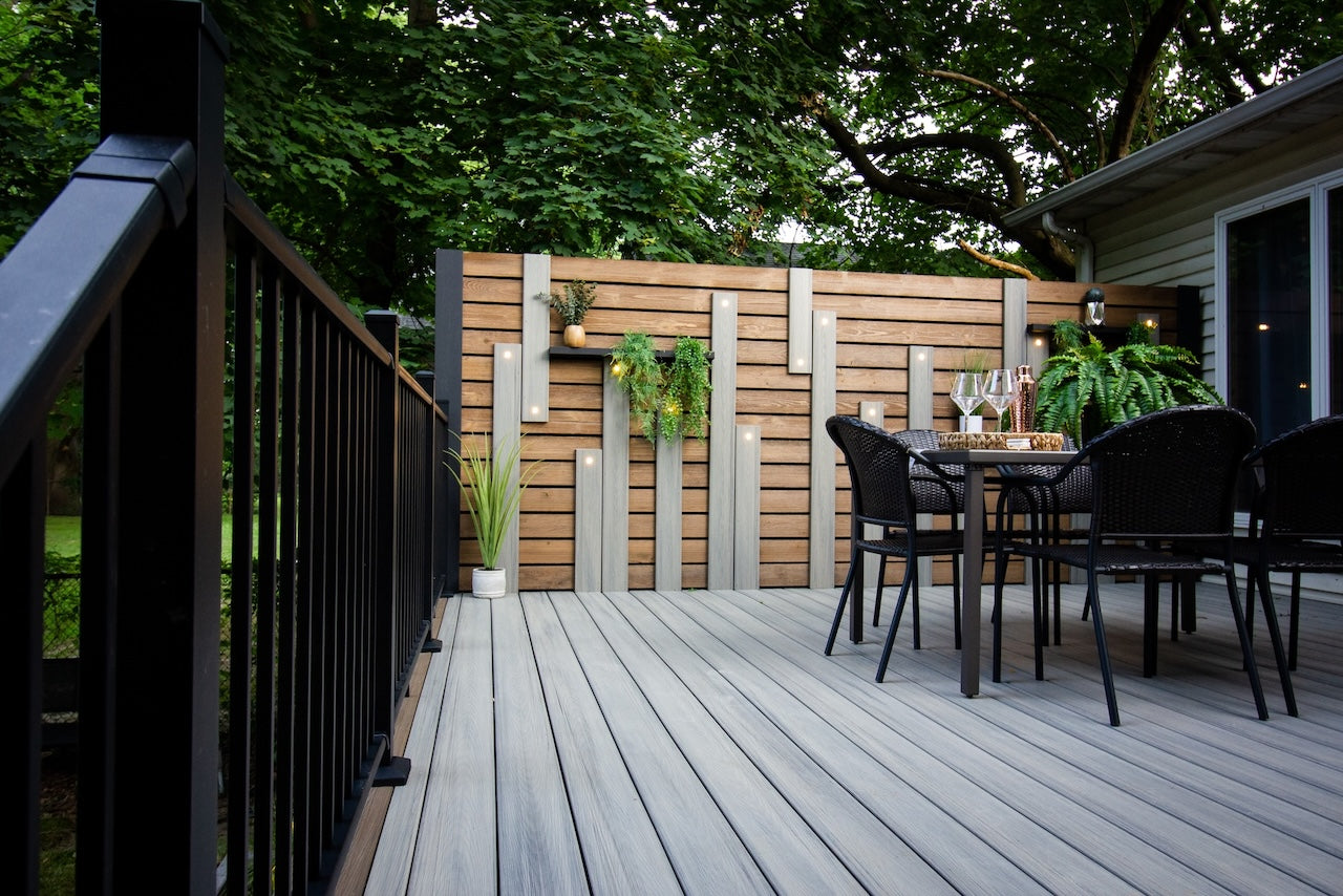 Gray deck with black railing and privacy wall with decorative boards featuring LED lights