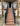 Outdoor composite staircase leading up to a house porch, with black metal railings and a wood-look deck surface. The stairs are installed in front of a beige stucco home with wooden support posts.