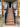 Outdoor composite staircase leading up to a house porch, with black metal railings and a wood-look deck surface. The stairs are installed in front of a beige stucco home with wooden support posts.